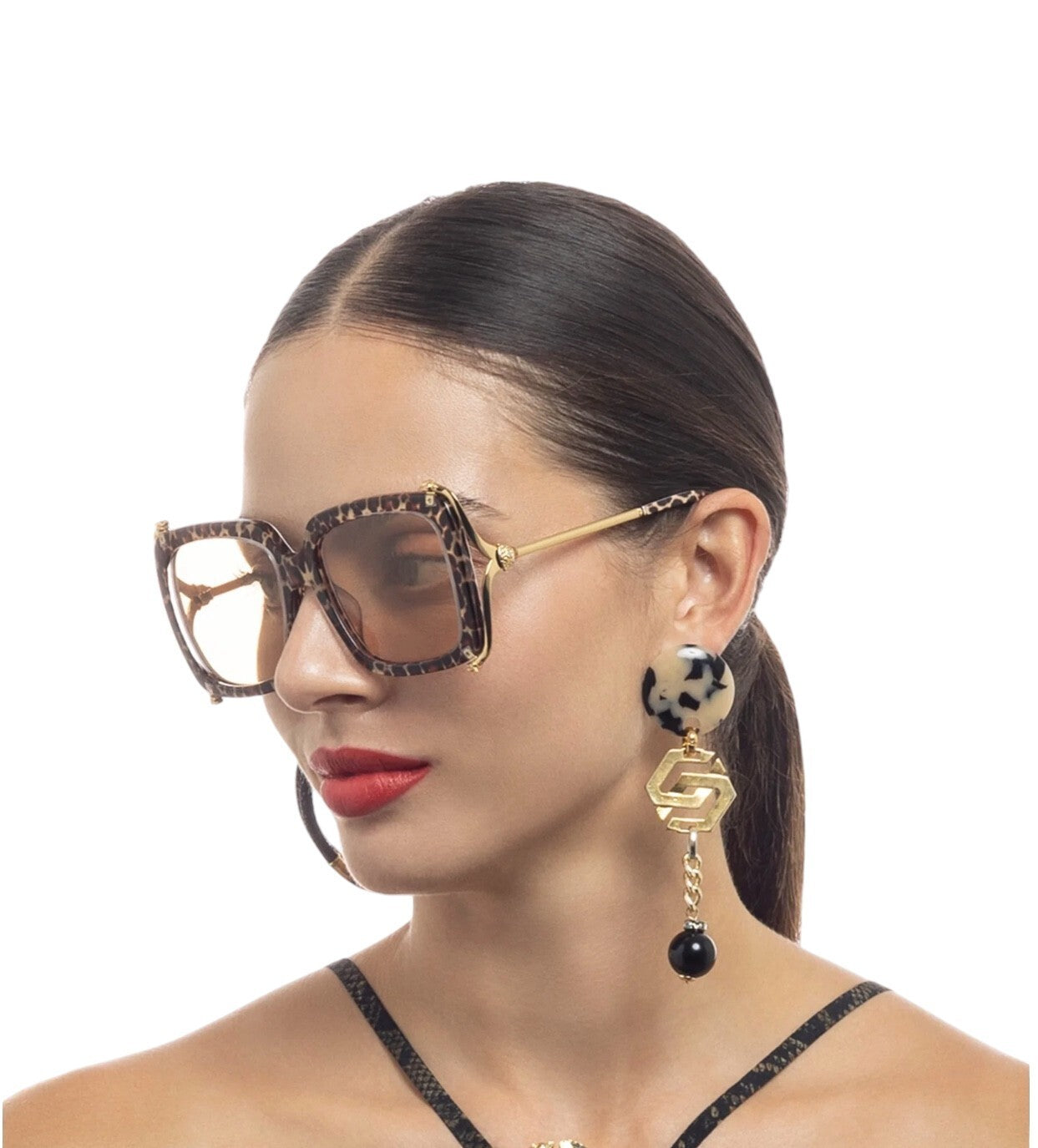 Woman wearing leopard print sunglasses and earrings on a white background