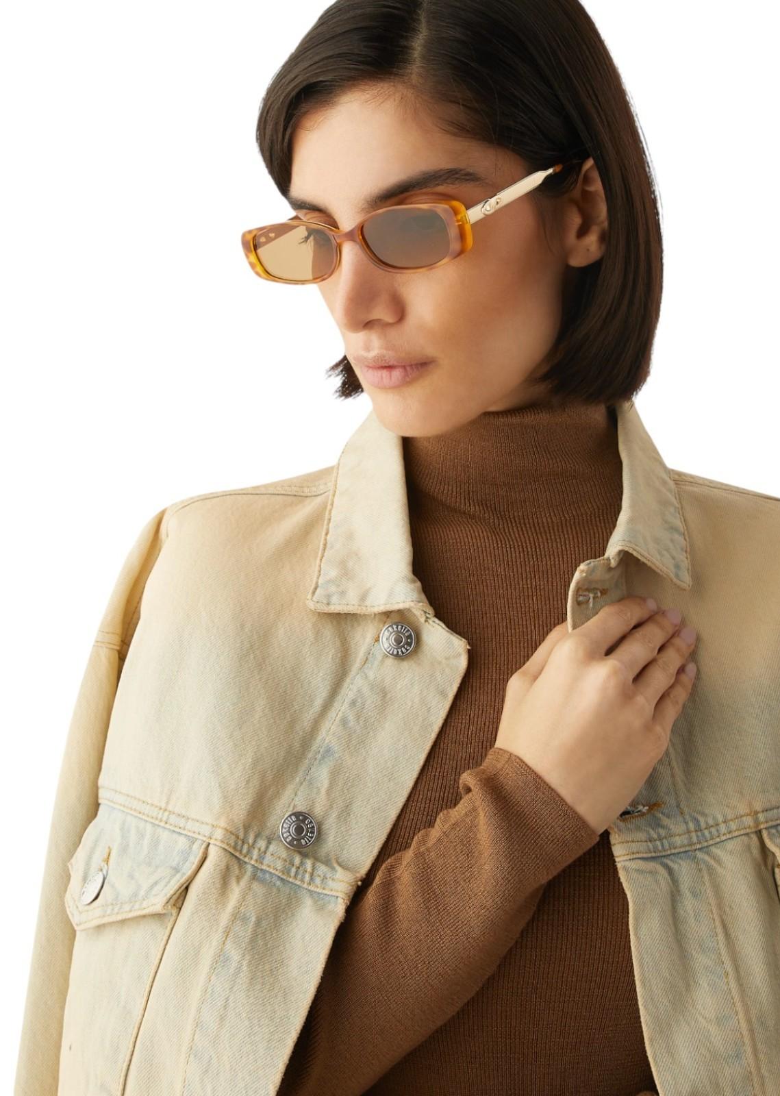 Woman wearing a beige jacket and brown turtleneck with sunglasses on a white background