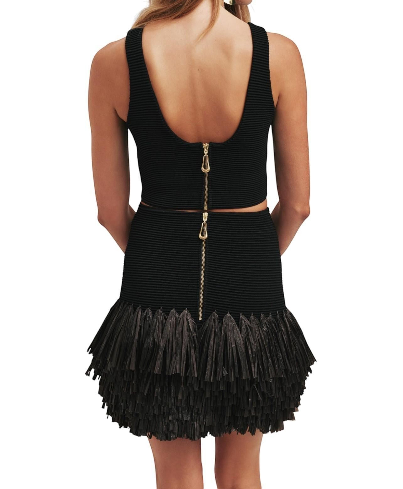 Naked Pear Aje black ribbed knit mini skirt with layered raffia hem and gold back zip detail on a model