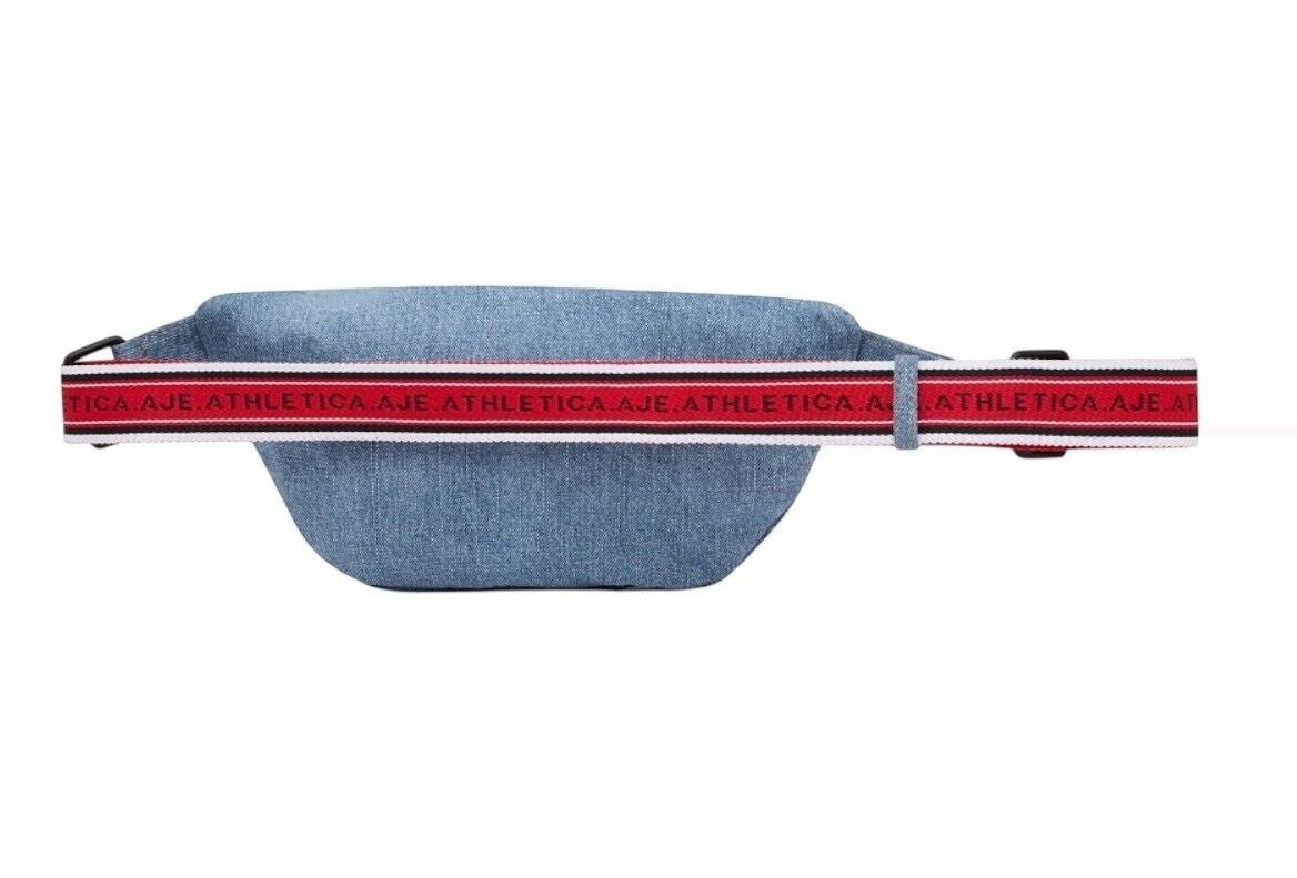 Naked Pear Aje Athletica denim crossbody bag in blue with an adjustable red, black, and white logo strap.