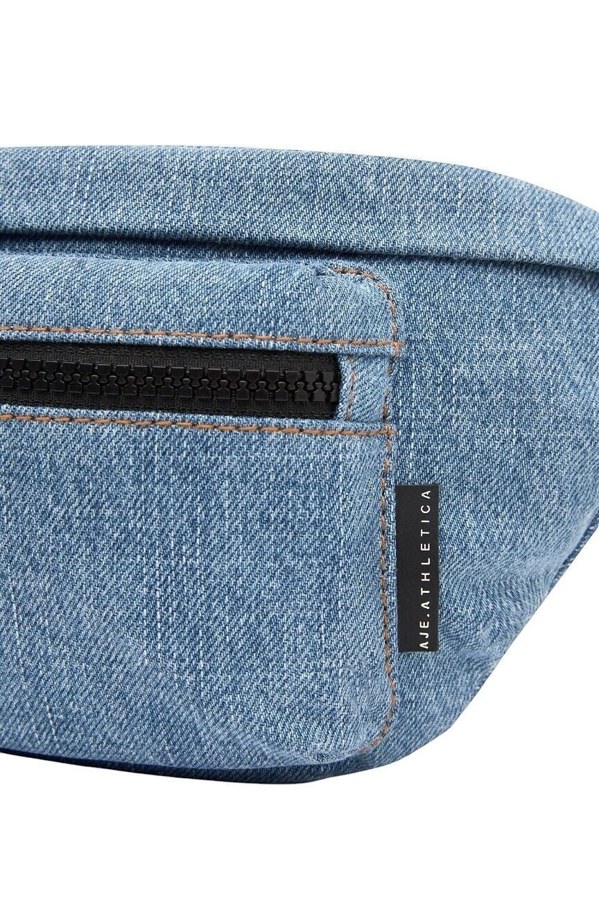 Naked Pear Aje. Athletica blue denim crossbody bag featuring a front zip pocket and matte black hardware detail.