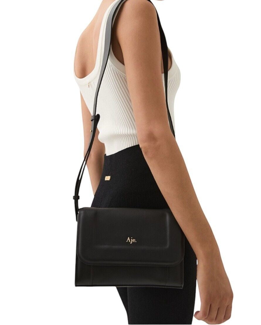 Naked Pear Aje Lora black cow leather crossbody bag with padded flap and gold logo worn by a model
