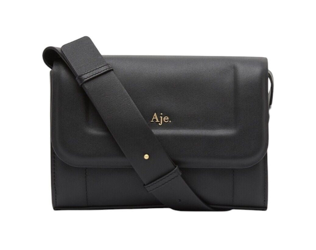 Naked Pear Aje Lora black cow leather crossbody bag with a padded flap, adjustable strap, and gold logo detail.