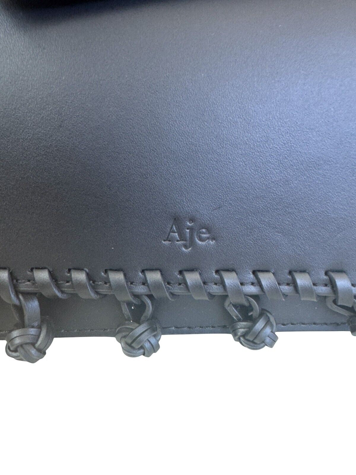 Naked Pear Aje black leather crossbody bag featuring a debossed logo and decorative leather pom-pom tassel trim.