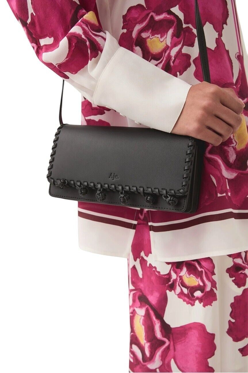 Naked Pear Aje black leather crossbody bag with tassel pom-pom trim and flap closure worn by a model