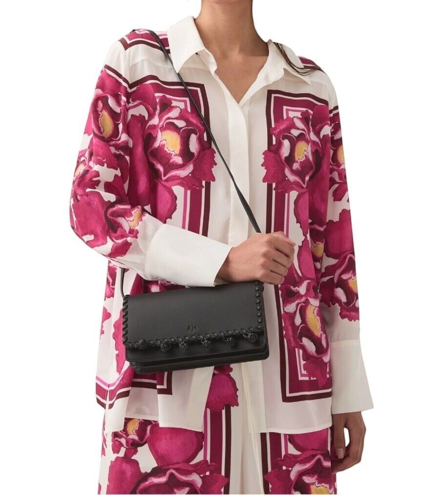 Naked Pear Aje black leather crossbody bag with pom-pom trim worn by a model in a floral shirt