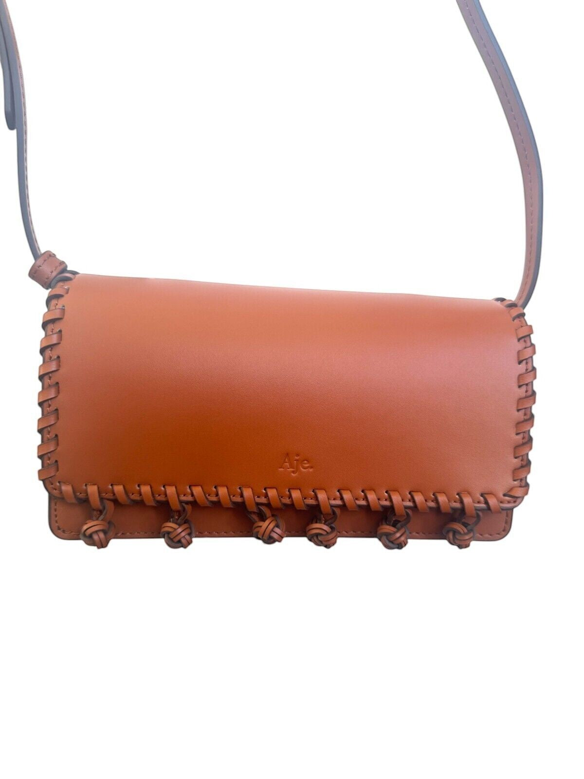 Naked Pear Aje Tasselate tan leather crossbody bag with whipstitch trim, pom-pom details, and magnetic flap closure.