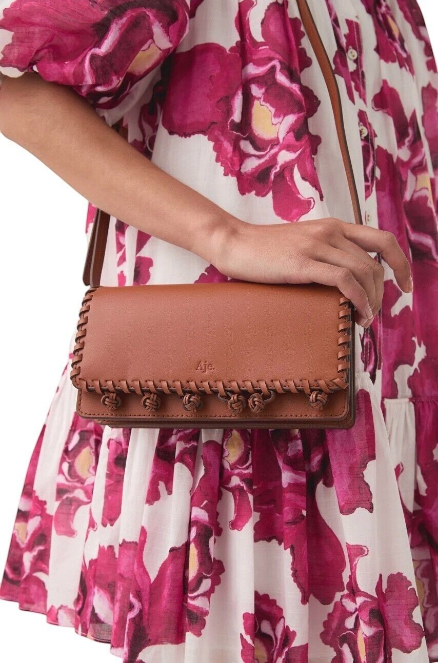 Naked Pear Aje tan leather crossbody bag with tassel pom-pom trim and magnetic flap closure worn by a model.