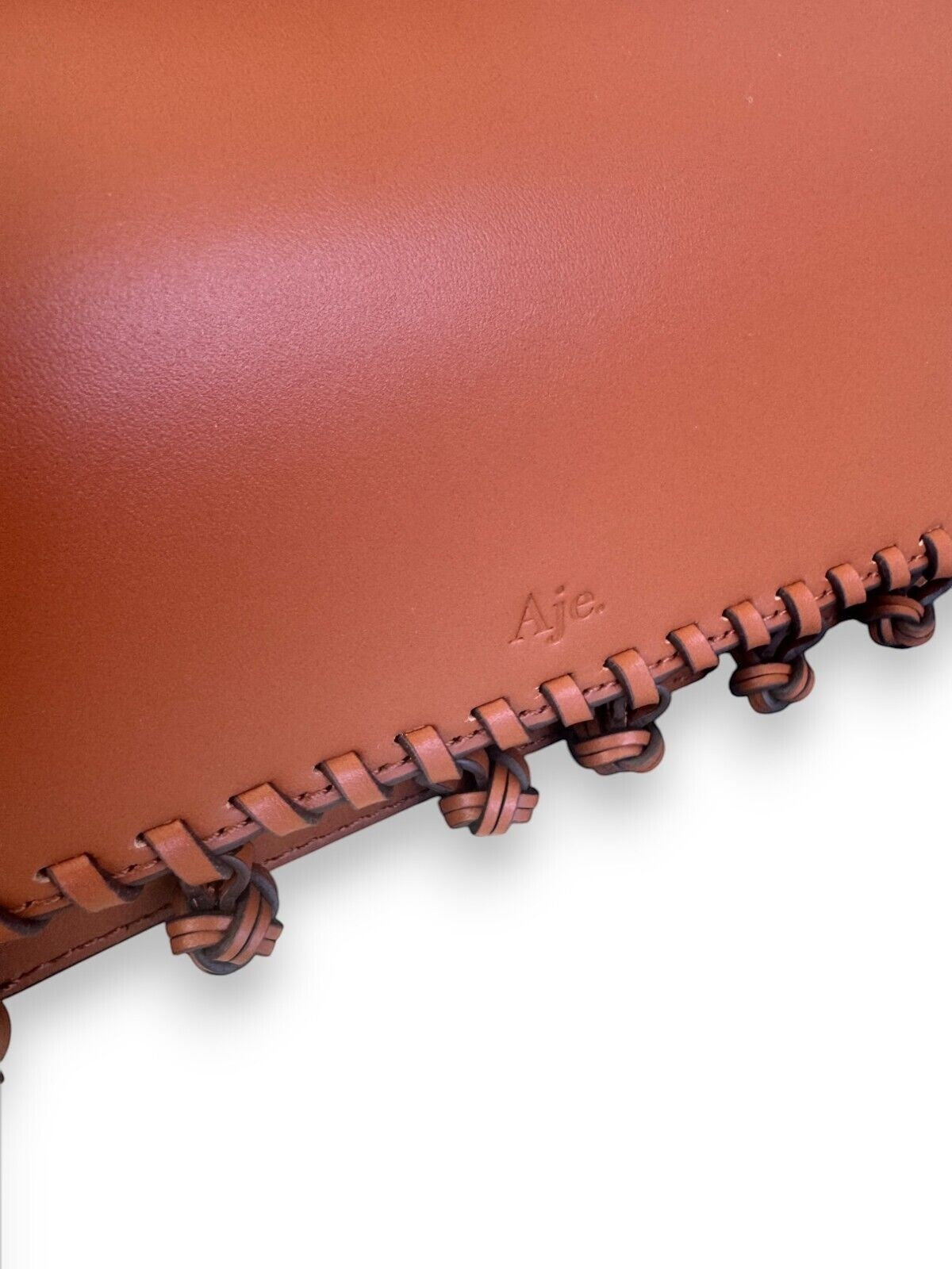 Naked Pear Aje Tasselate tan leather crossbody bag featuring a debossed logo and decorative knotted leather trim.