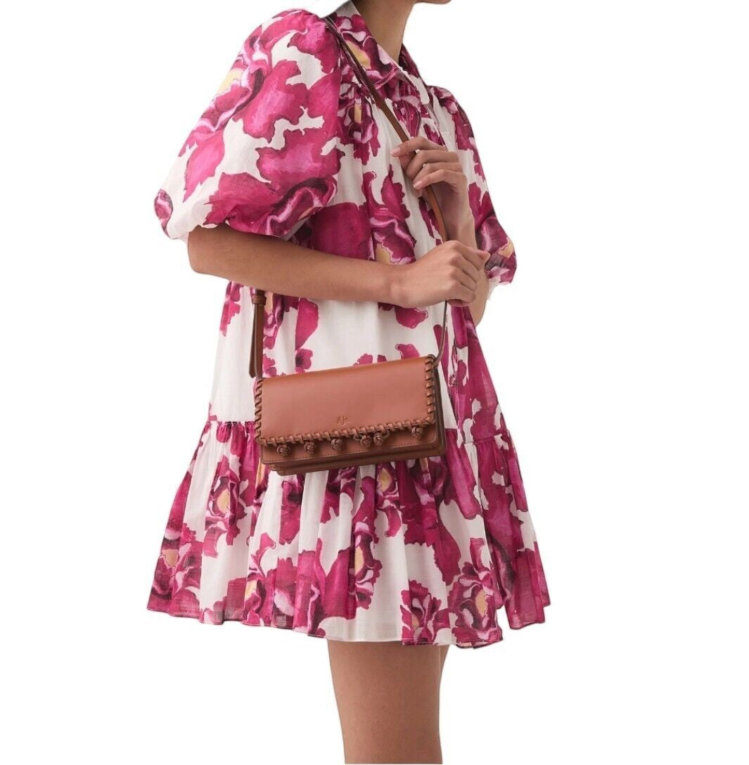 Naked Pear Aje tan leather crossbody bag with pom-pom trim worn by a model in a floral dress