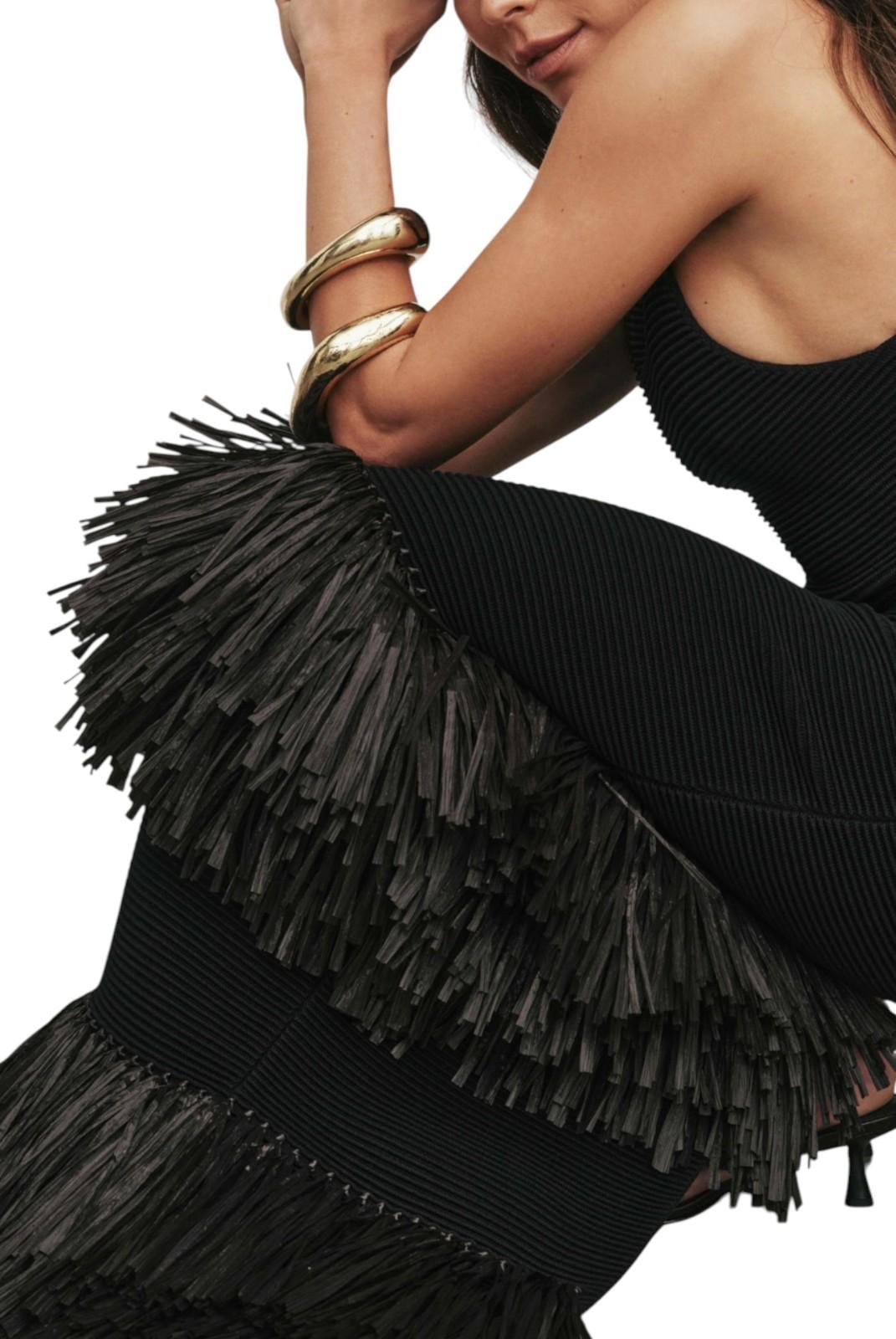 Person wearing a black fringe dress with gold jewelry on a white background