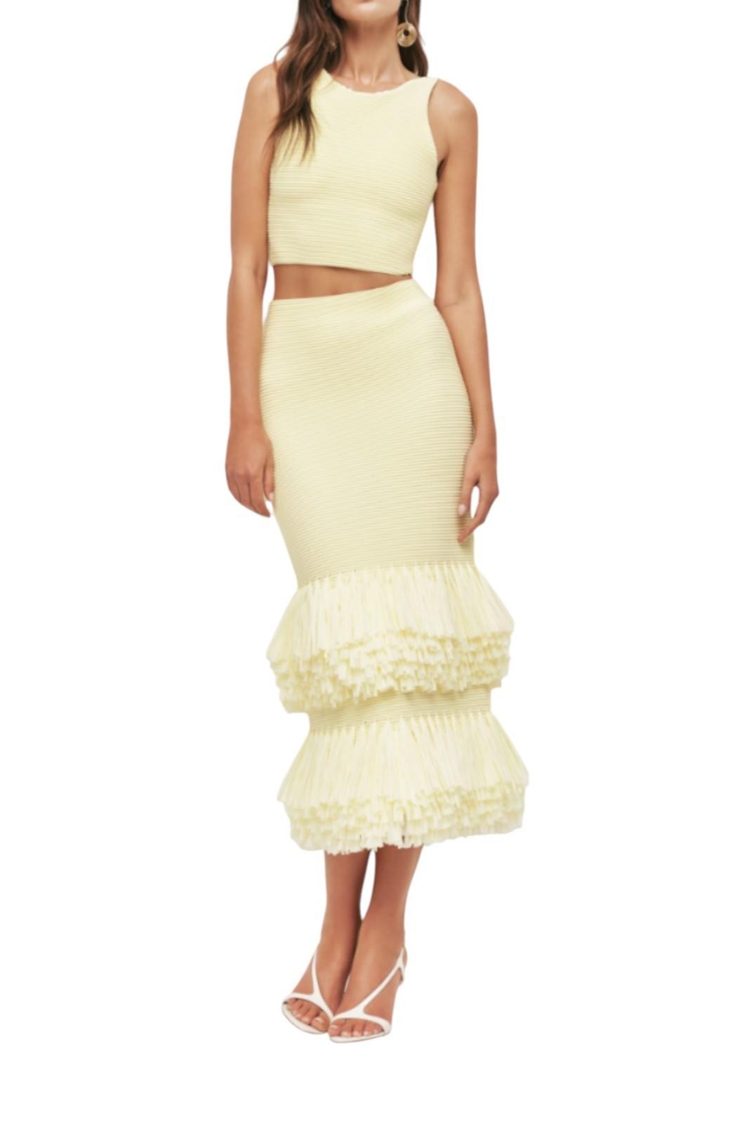 Woman wearing a light yellow two-piece outfit with a top and ruffled skirt on a white background