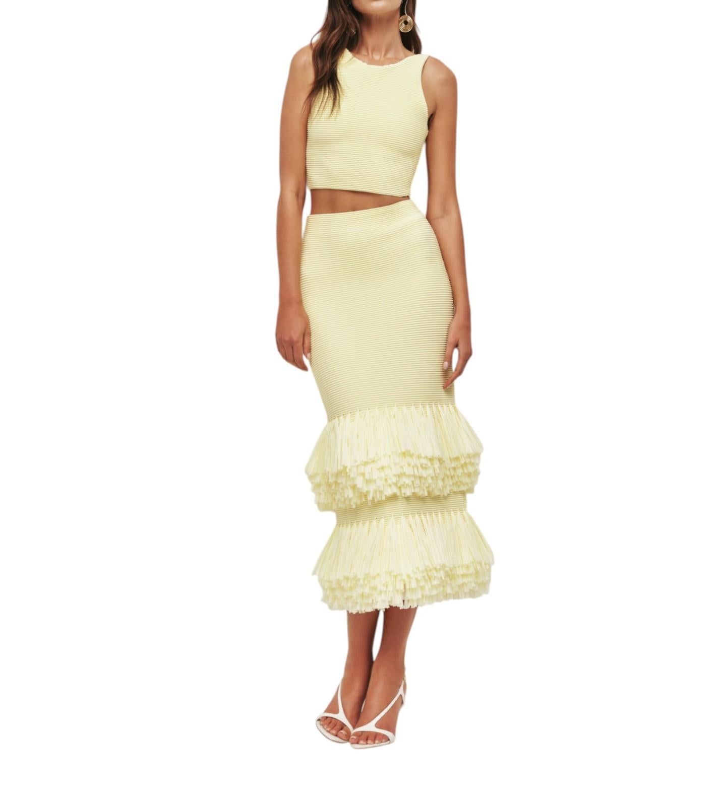 Woman wearing a light yellow two-piece outfit with a ruffled skirt on a white background