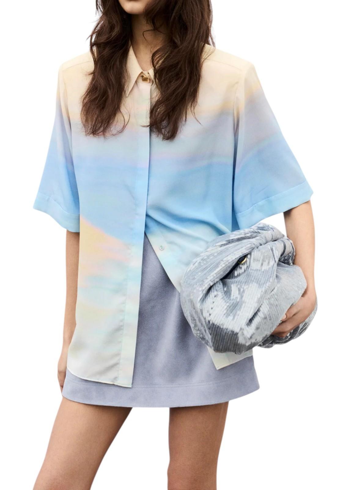 Woman wearing a colorful shirt and holding a gray clutch against a white background