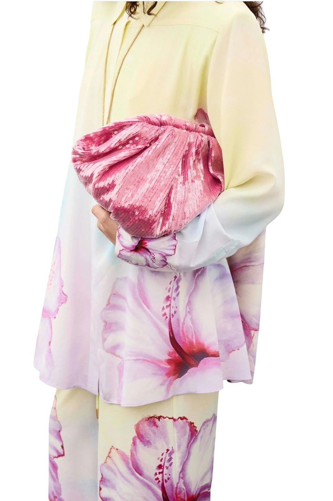 Person wearing a light-colored outfit with a pink floral pattern, holding a pink clutch.