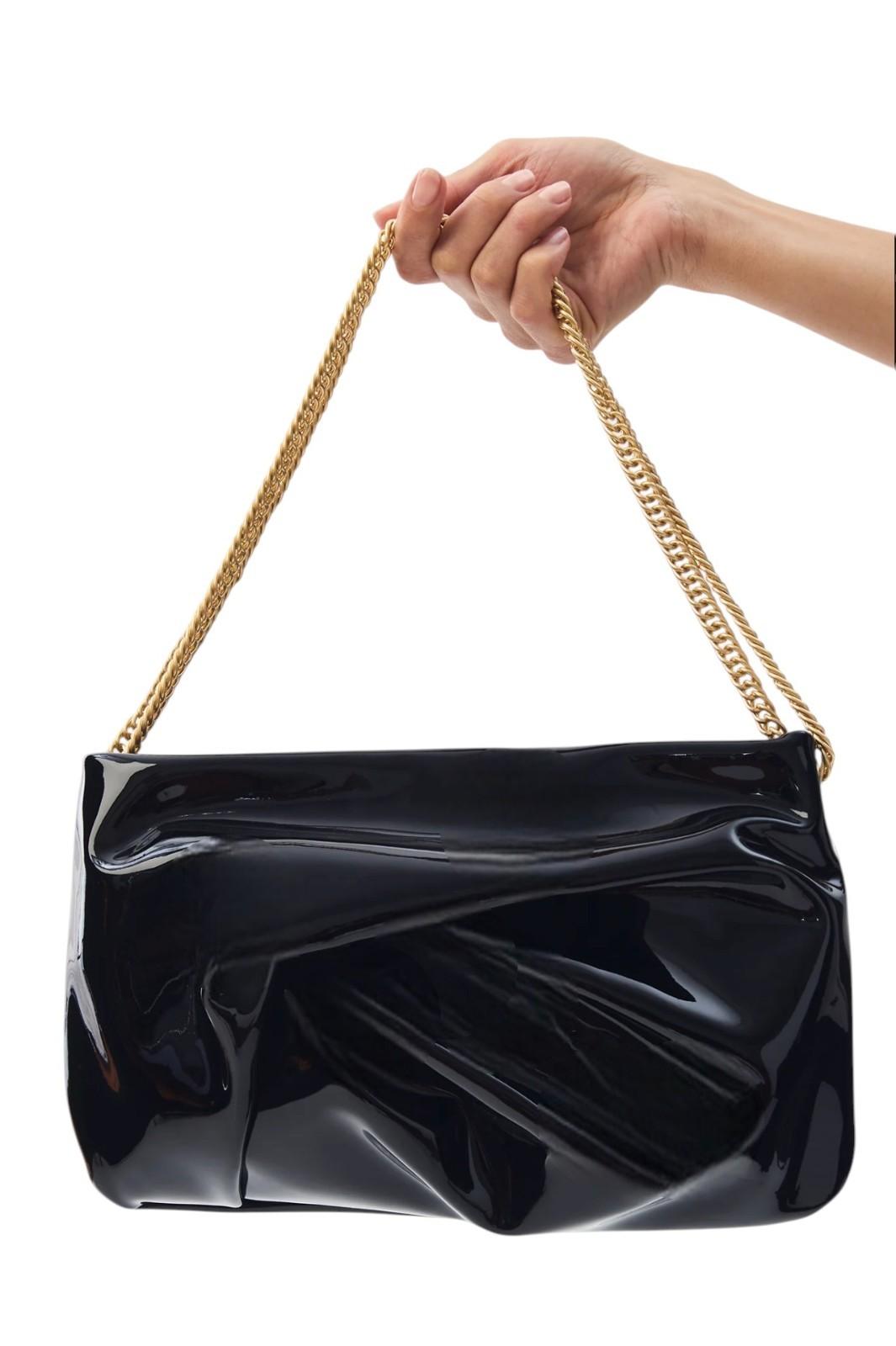 Black handbag with gold chain handle held by a hand on a white background