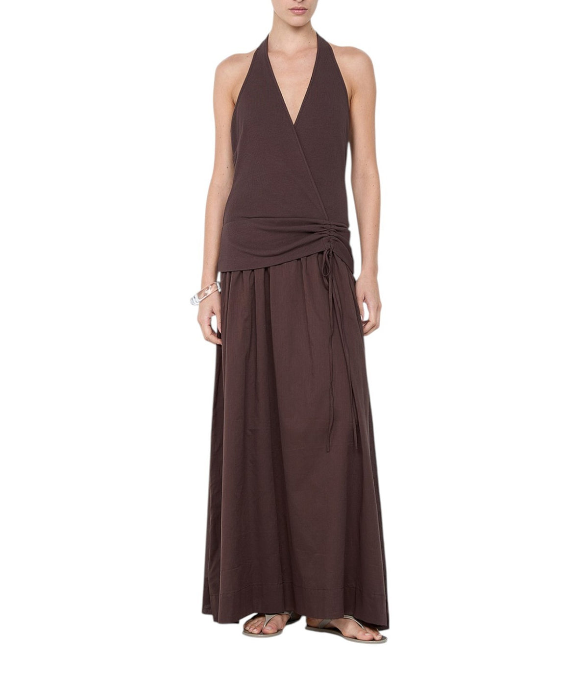 A woman modeling a dark brown halter-neck maxi dress with a wrap-style bodice and side tie, shown against a plain white background.