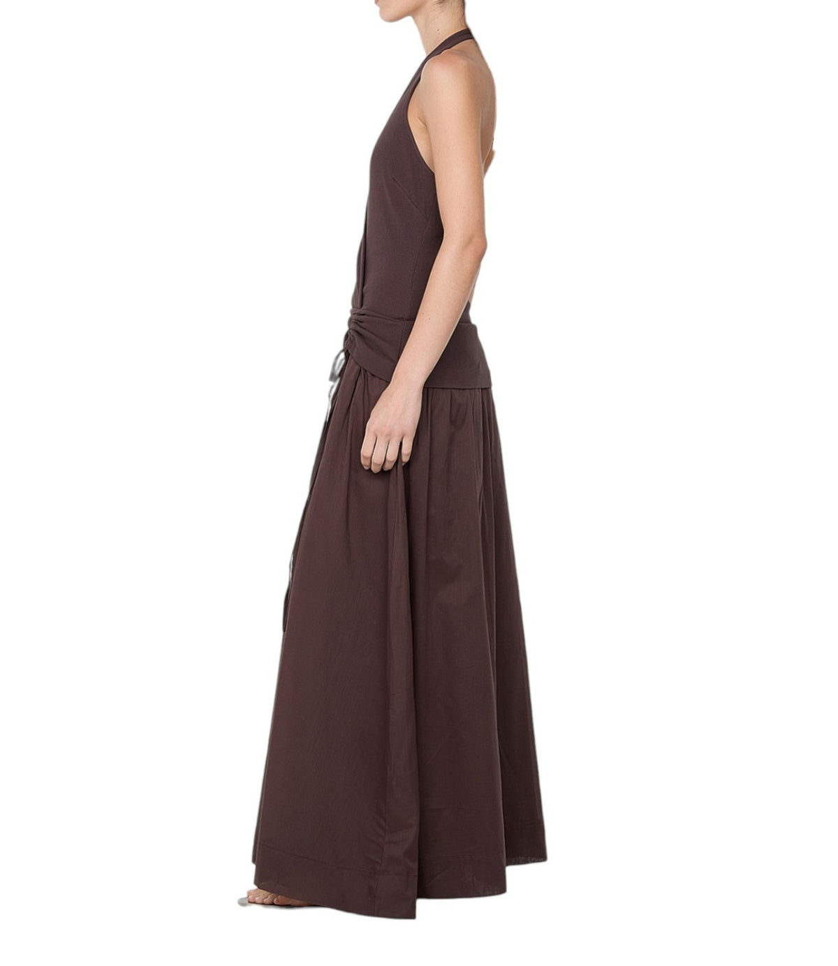 A woman shown in side profile wearing a dark brown sleeveless maxi dress with a tie-waist detail, photographed against a plain white background.