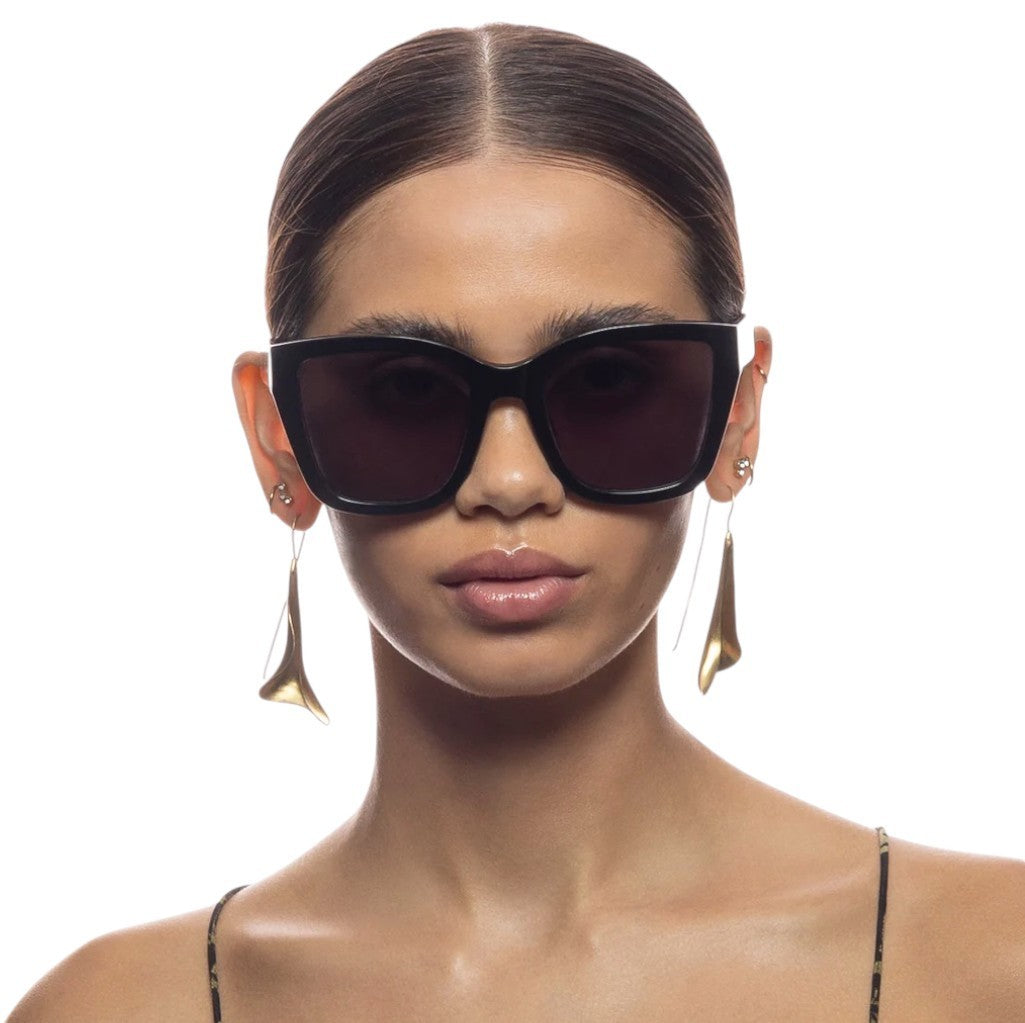 Woman wearing dark sunglasses and gold earrings on a white background