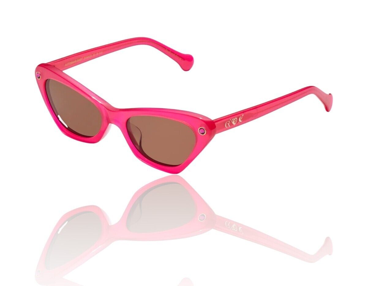 A pair of pink, cat-eye style sunglasses with brown lenses and a signature gold foil icon trio on the temples, featuring a small frame and plant-based acetate material.