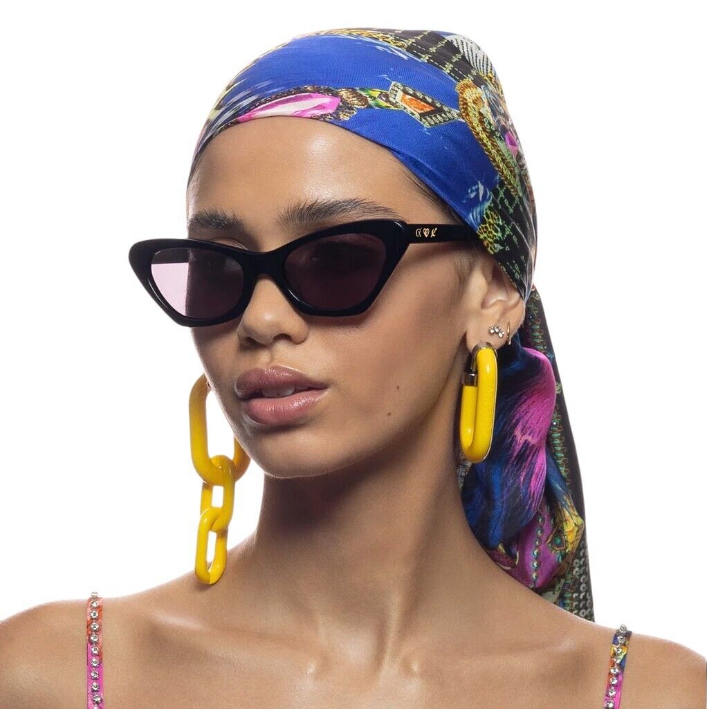 A woman wearing sunglasses with a small navy blue patterned scarf and large yellow hoop earrings.