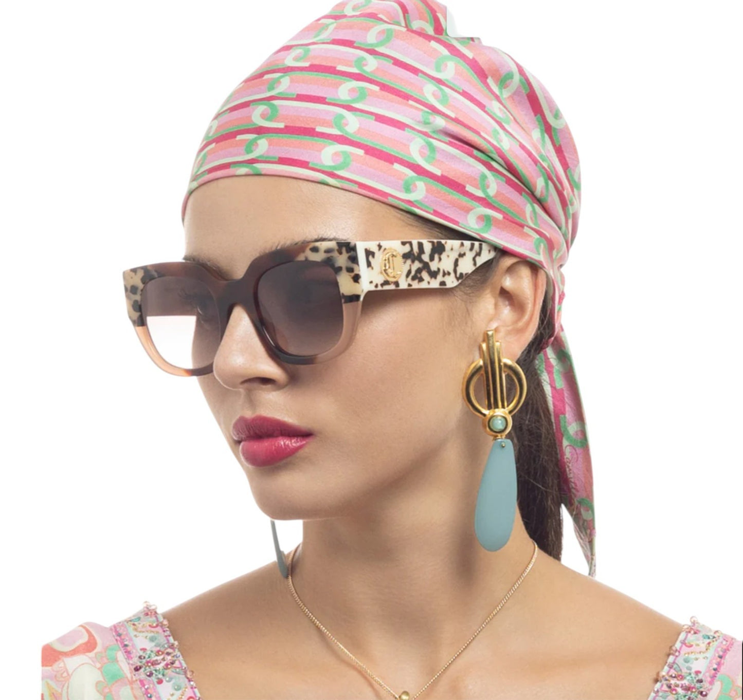 Woman wearing a colorful headscarf, sunglasses, and earrings on a white background