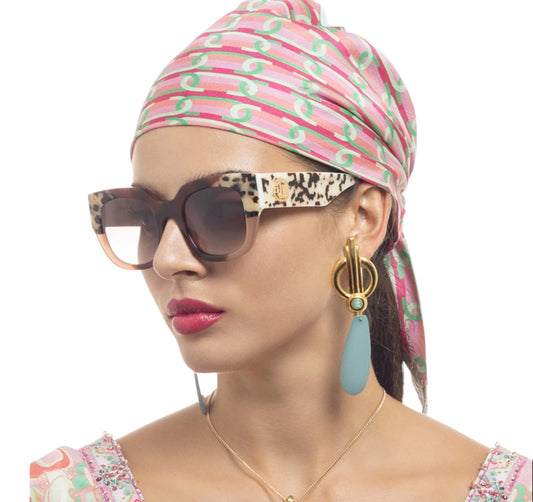 Woman wearing a colorful headscarf, sunglasses, and earrings on a white background