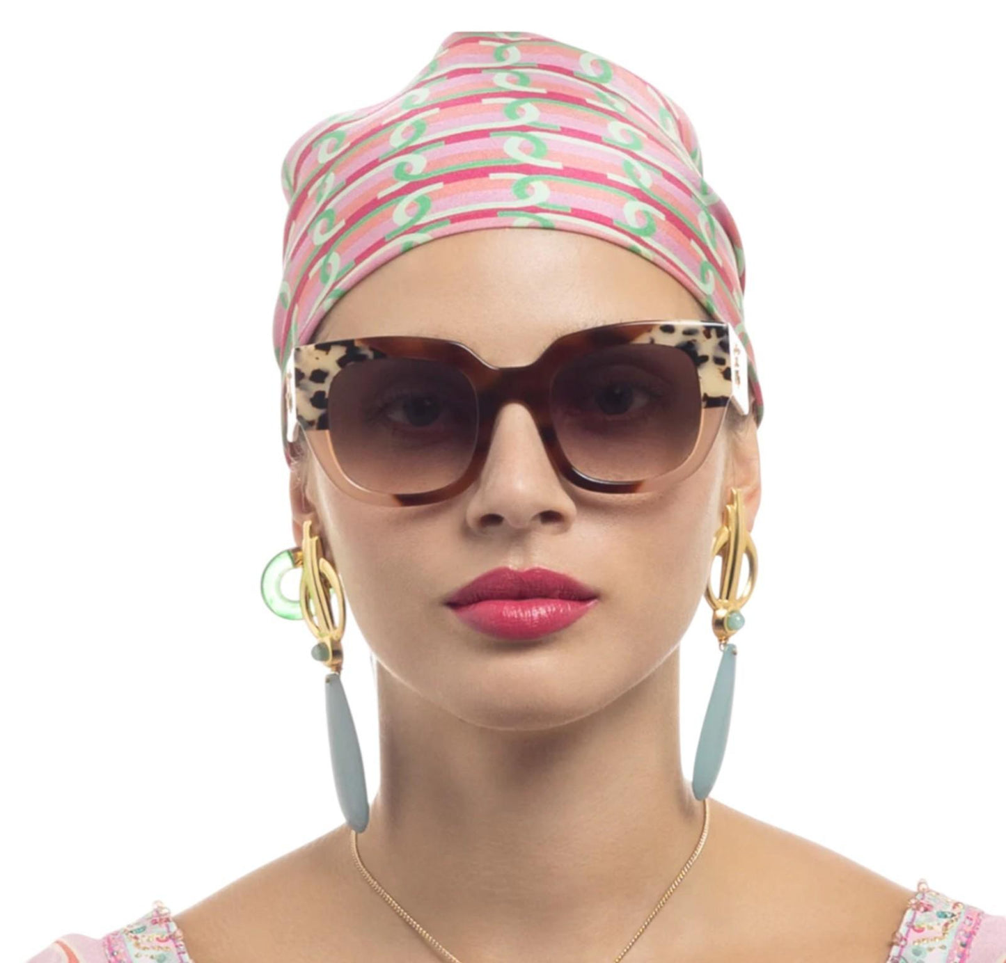 Woman wearing a colorful headscarf, sunglasses, and earrings on a white background