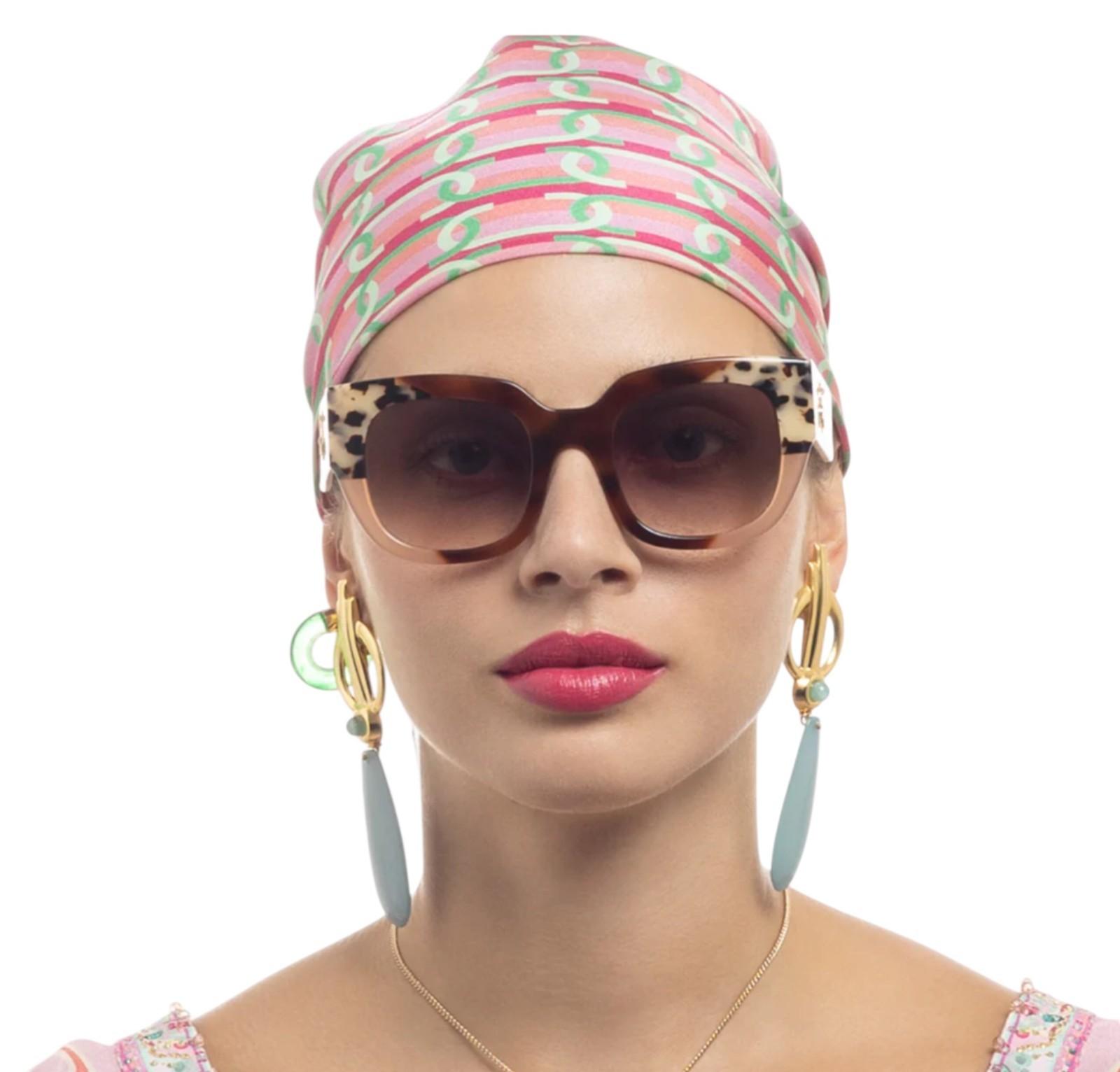Woman wearing a colorful headscarf, sunglasses, and earrings on a white background