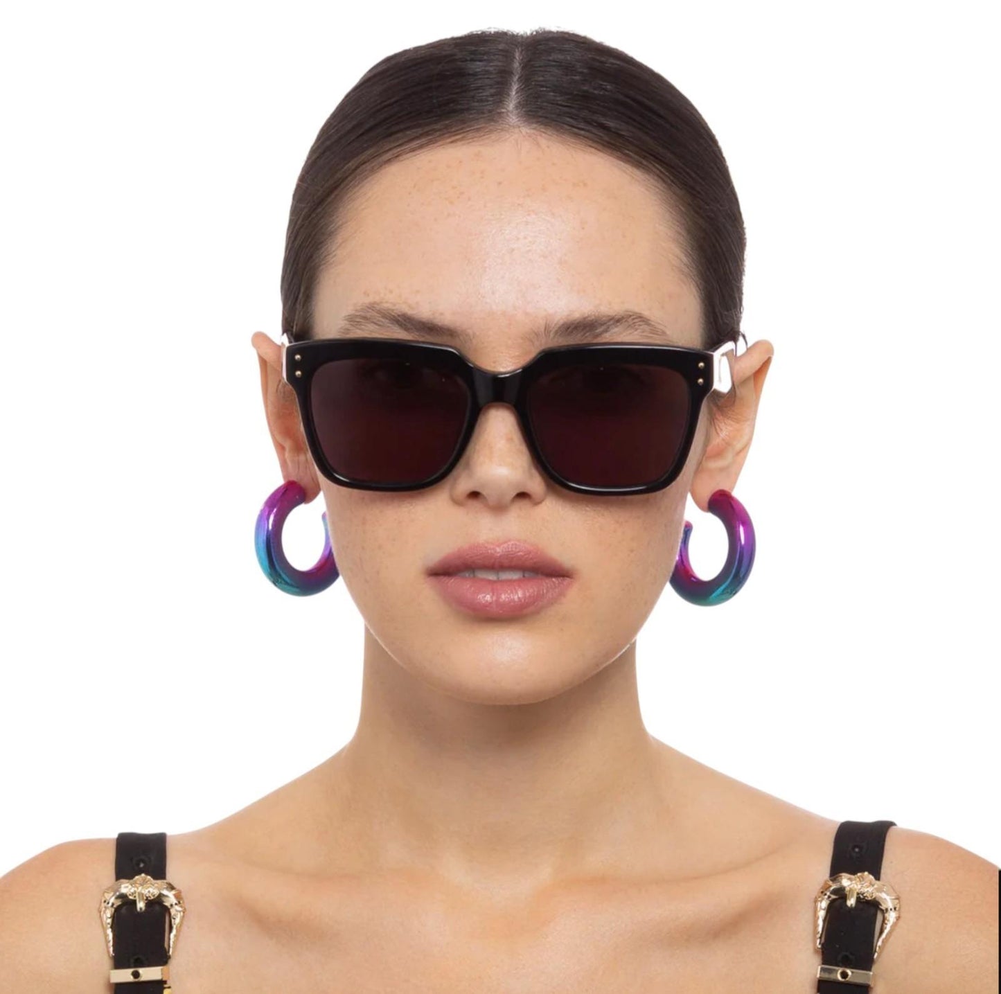 Woman wearing black sunglasses with colorful hoop earrings on a white background