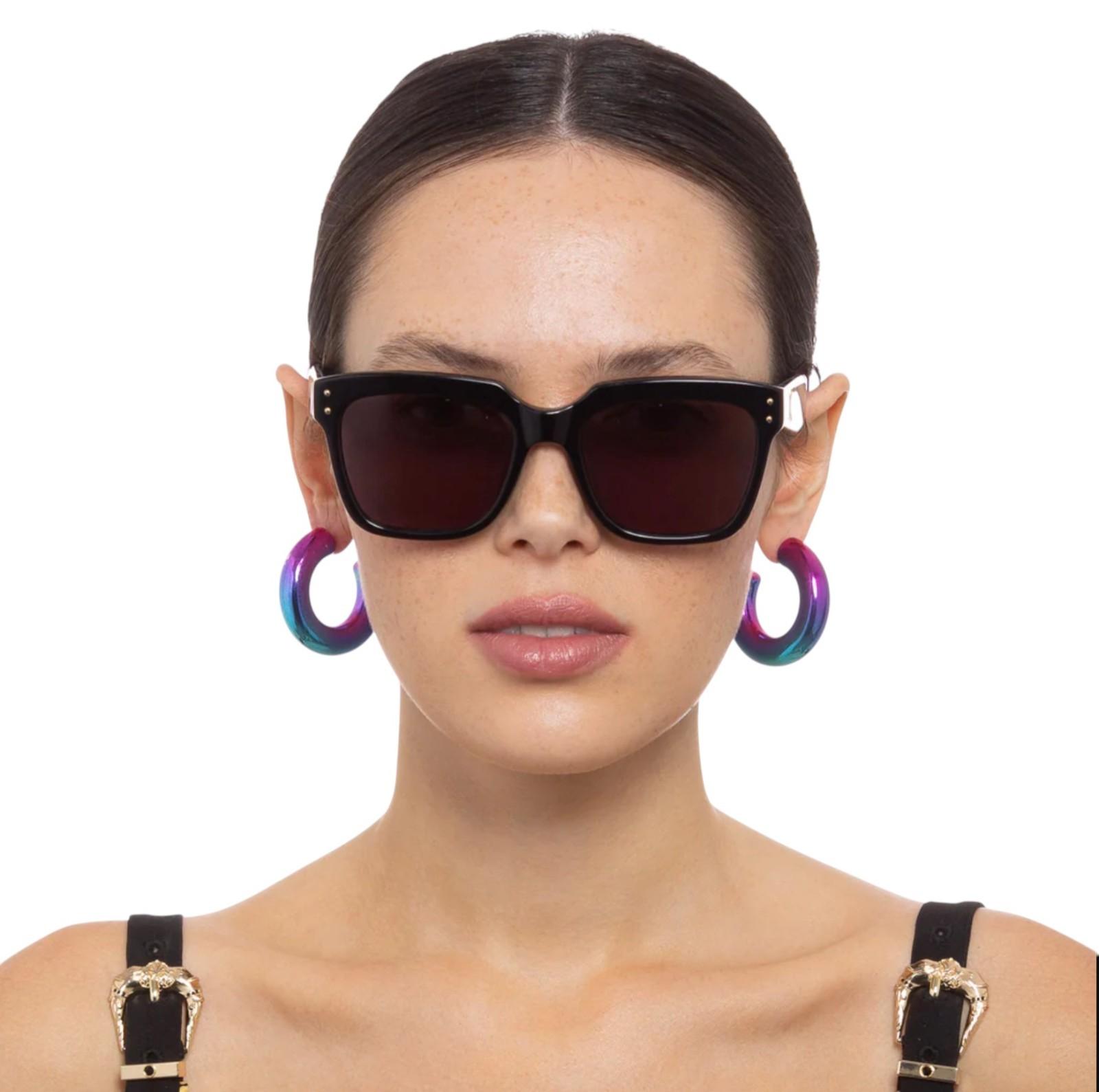Woman wearing black sunglasses with colorful hoop earrings on a white background