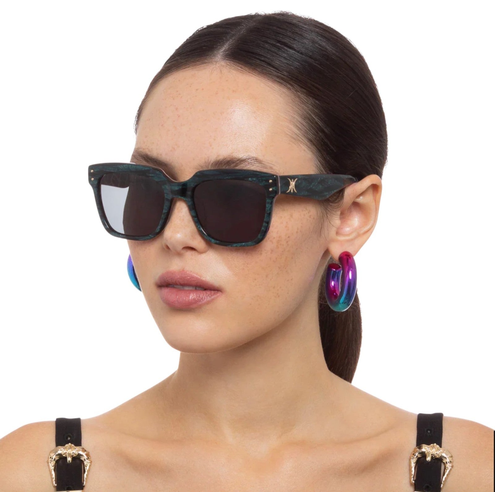 Woman wearing dark sunglasses and colorful hoop earrings on a white background