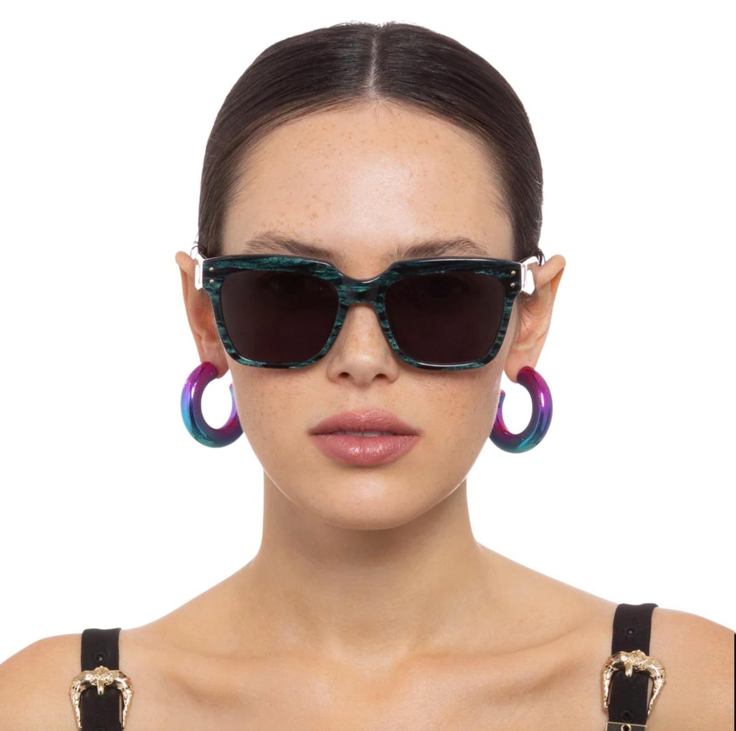 Woman wearing a pair of sunglasses with colorful hoop earrings on a white background