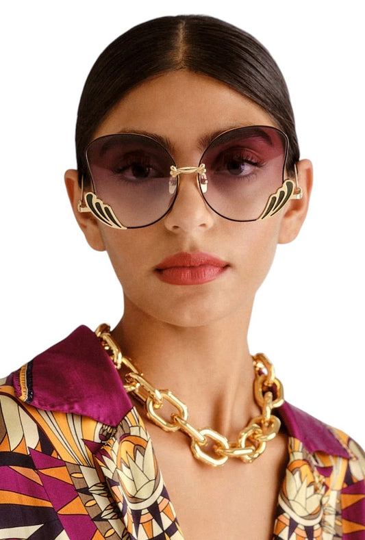 Woman wearing a gold chain necklace and sunglasses with a patterned shirt.