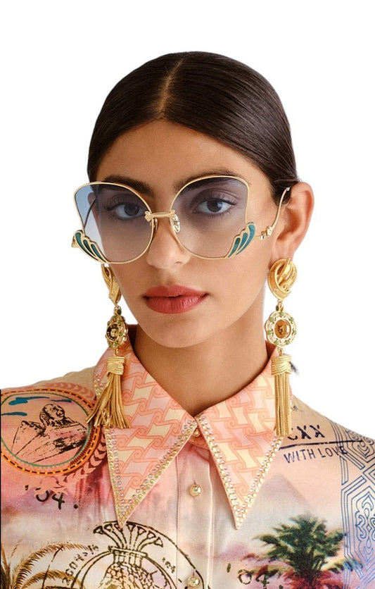 Woman wearing gold sunglasses and earrings with a colorful patterned shirt.