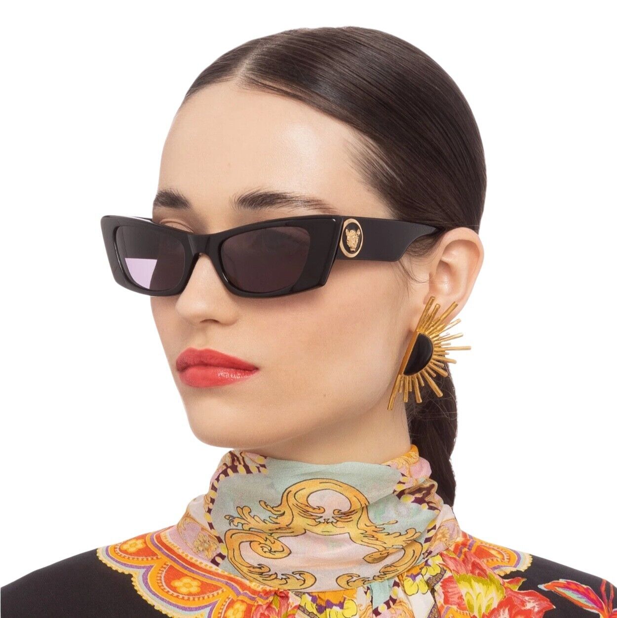 A woman wearing black acetate sunglasses with gold detailing and a floral scarf.