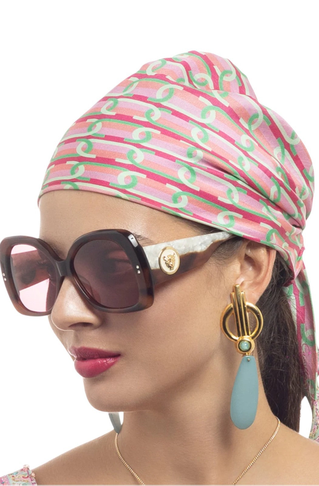 Woman wearing a patterned headscarf, sunglasses, and earrings on a white background