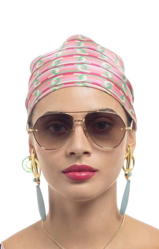 Woman wearing a patterned headscarf, sunglasses, and earrings on a white background