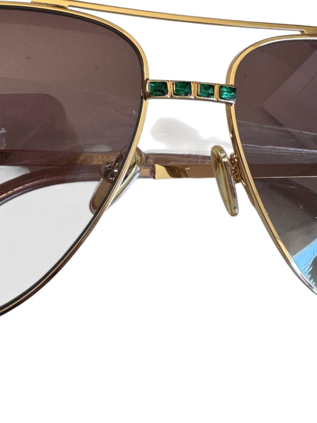 Gold-framed sunglasses with emerald accents on a white background