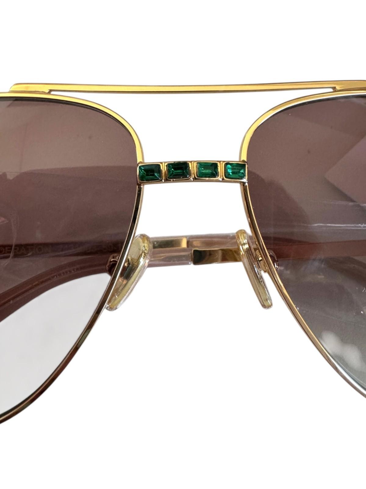 Gold-framed sunglasses with emerald accents on a white background