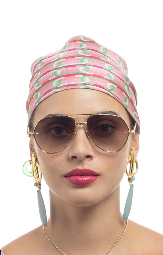 Woman wearing a patterned headscarf, sunglasses, and earrings on a white background
