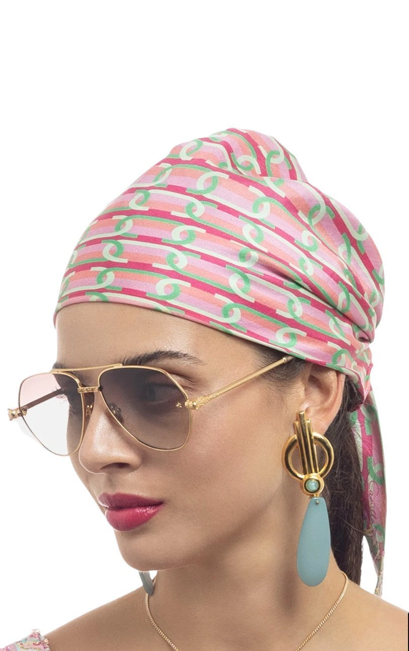 Woman wearing a pink patterned headscarf, sunglasses, and large earrings on a white background