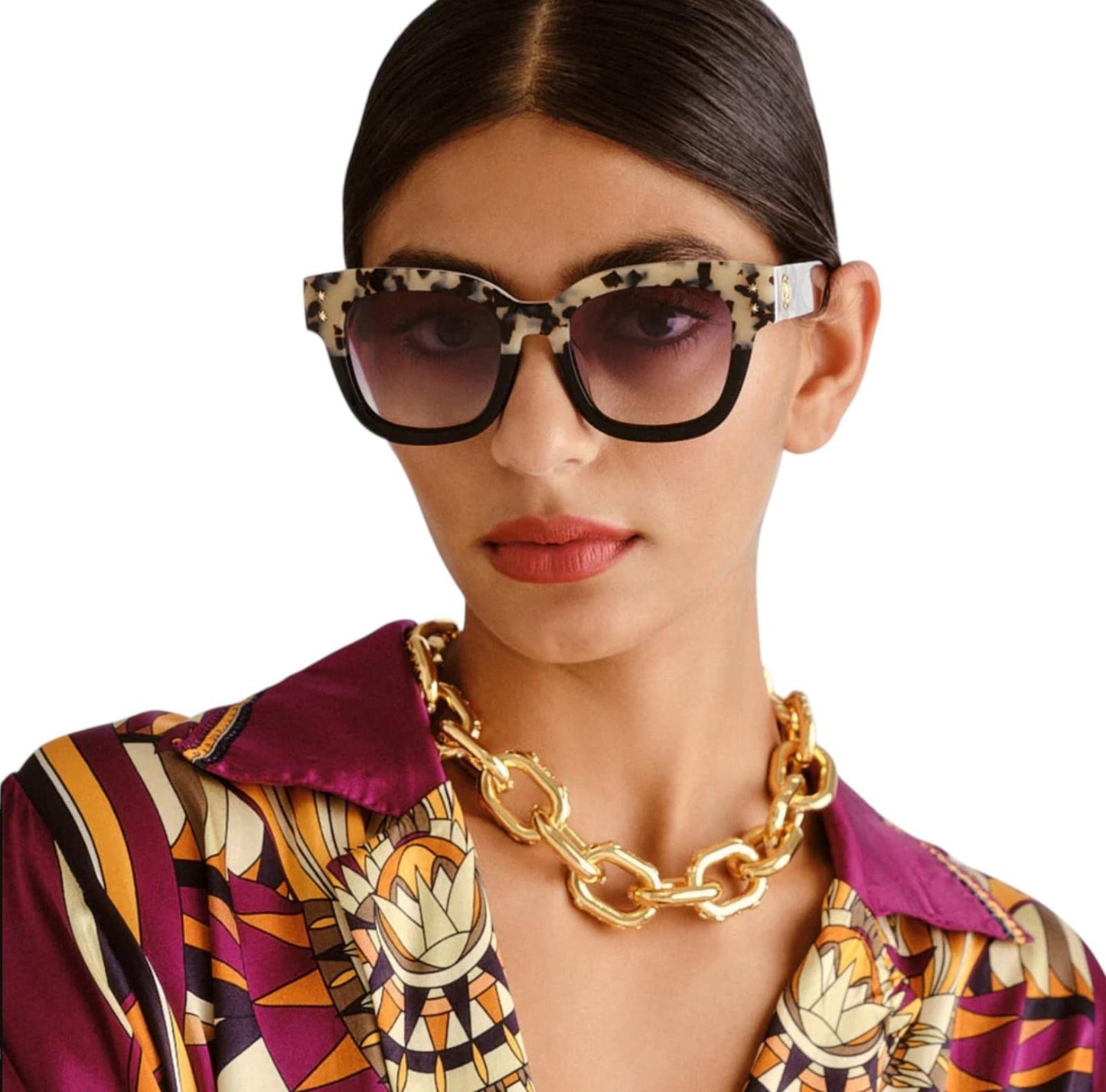 Woman wearing a patterned shirt and gold necklace with sunglasses on a white background