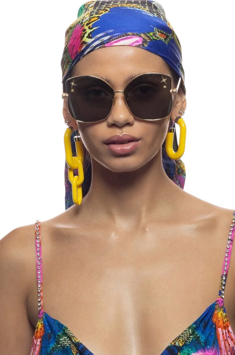 Woman wearing sunglasses, colorful headscarf, and earrings on a white background
