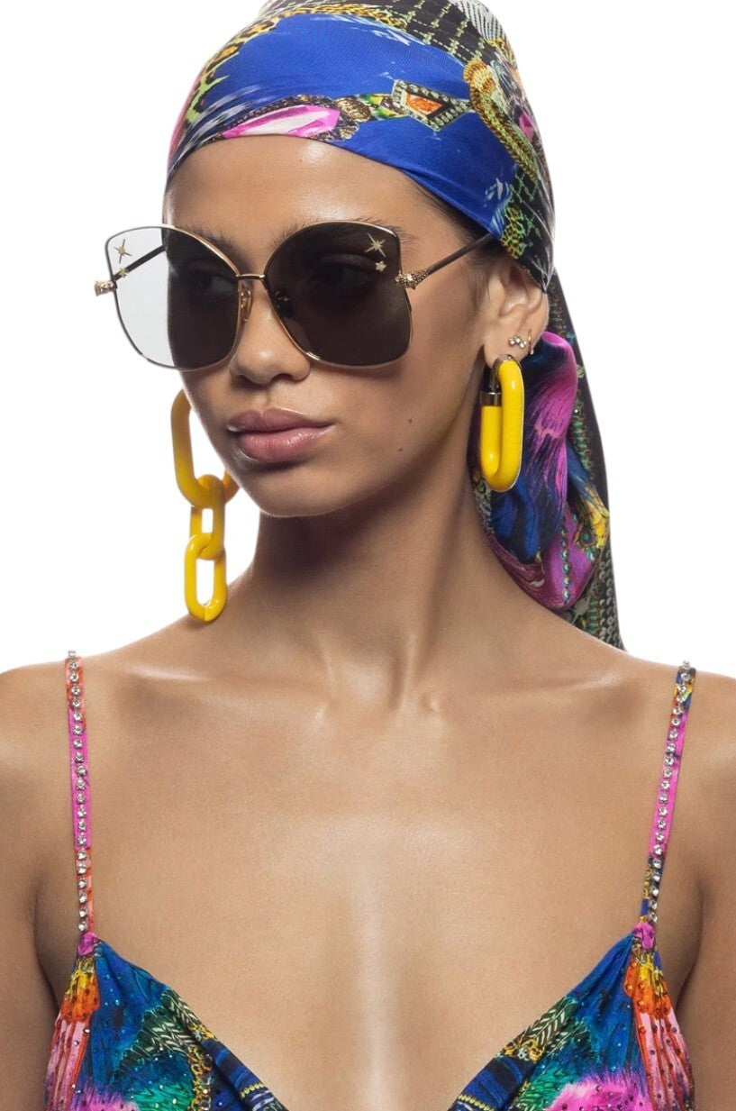 Woman wearing a colorful headscarf, sunglasses, and earrings on a white background