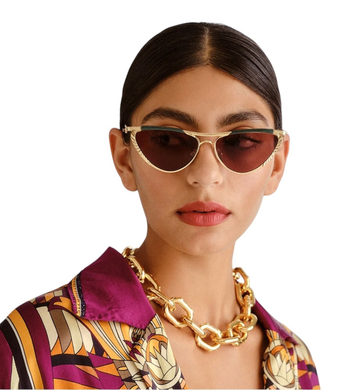 Woman wearing gold sunglasses and a patterned shirt with a gold necklace on a white background