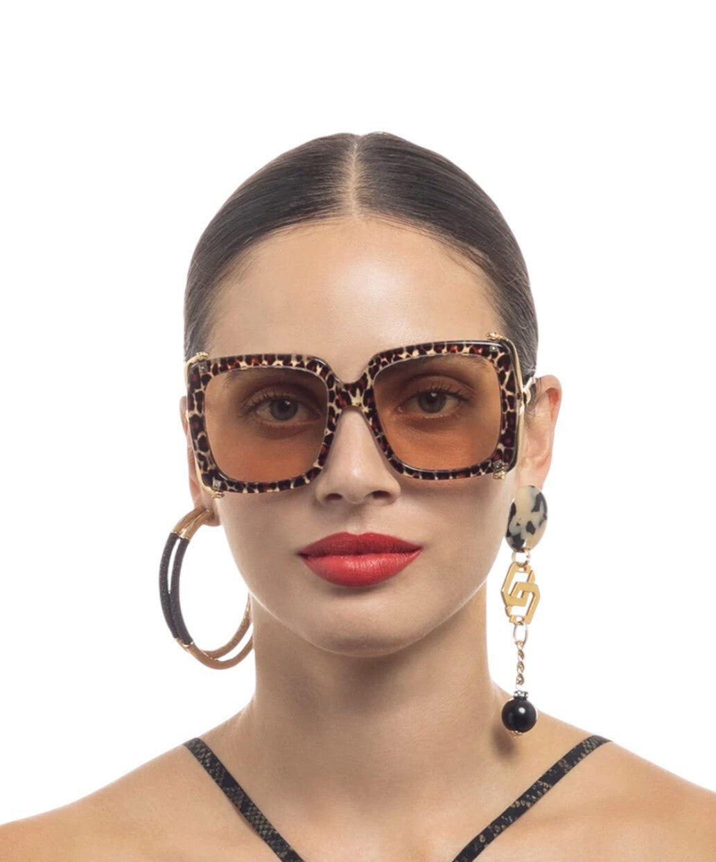 Woman wearing leopard print sunglasses and earrings on a white background