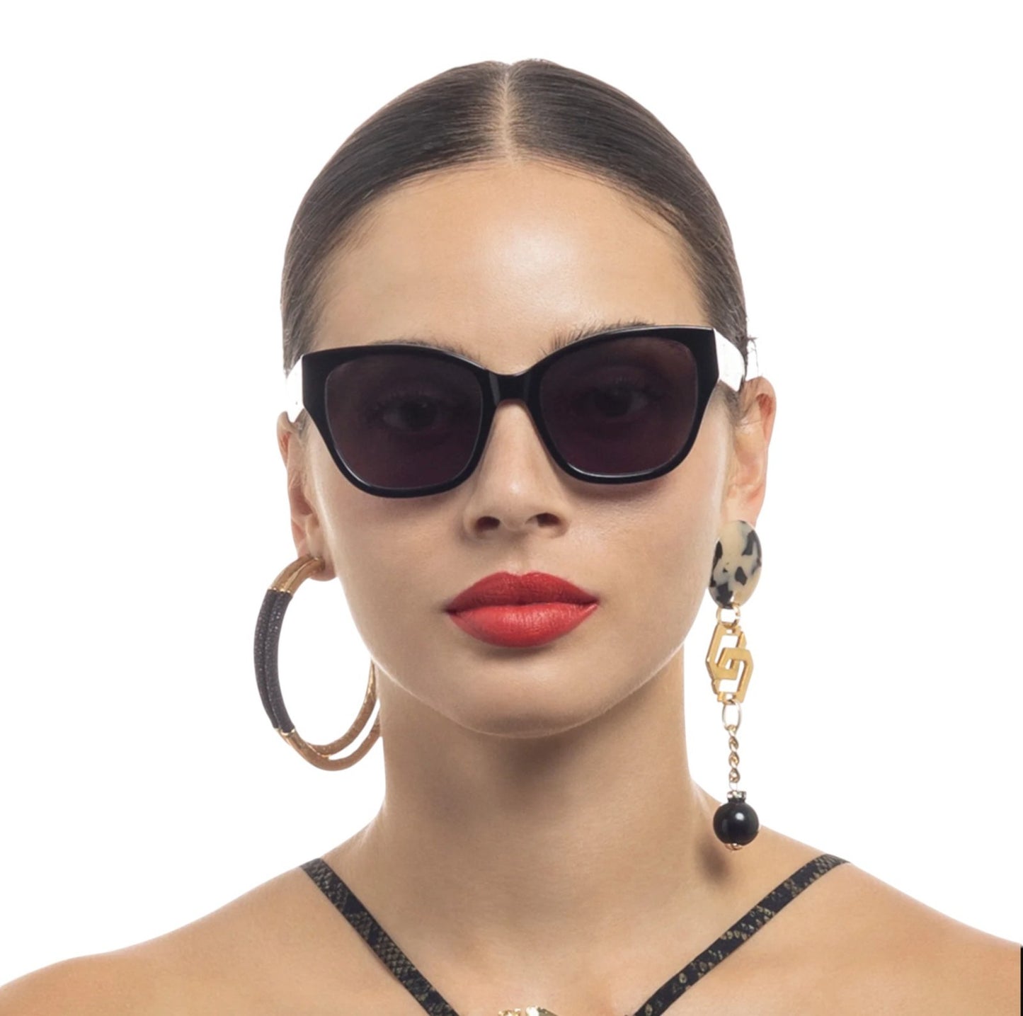Woman wearing dark sunglasses and hoop earrings on a white background