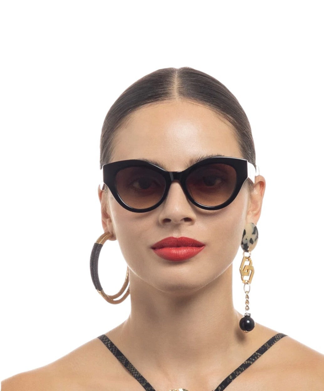 Woman wearing black cat-eye sunglasses and hoop earrings on a white background