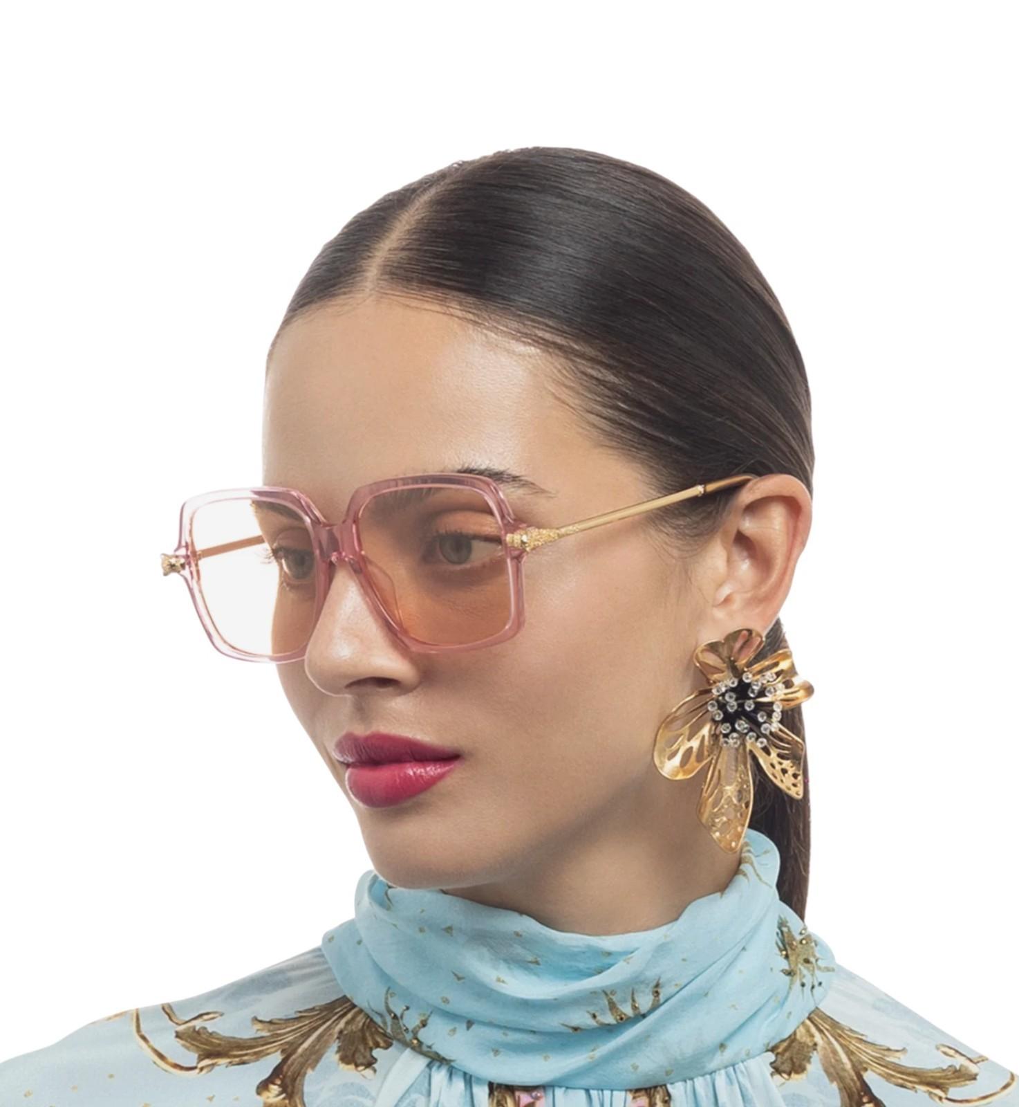 Woman wearing pink sunglasses and gold earrings with a light blue scarf